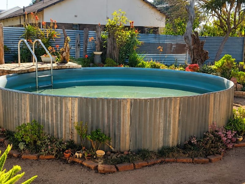 An above-ground circular pool featuring corrugated metal siding, a metal ladder, and stone decking, set within a landscaped garden area.