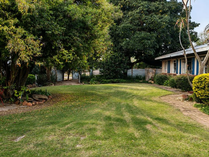 A spacious, well-established garden featuring mature trees, a manicured lawn, and a brick pathway leading alongside the property.