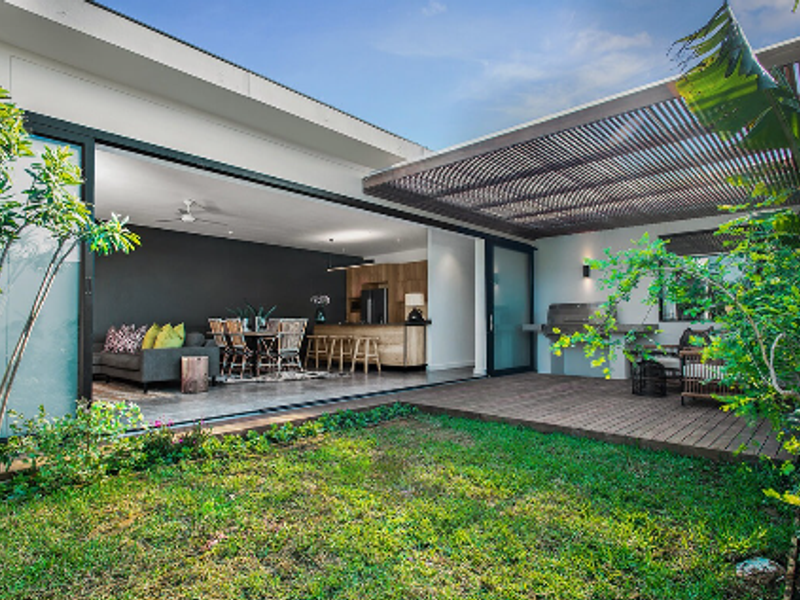Modern outdoor patio featuring timber decking, a slatted pergola, and a built-in barbecue, seamlessly connecting to the open-plan interior living and kitchen area.