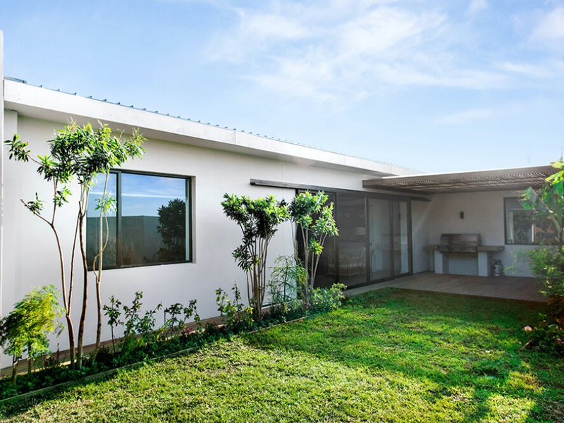 Rear exterior view featuring a landscaped garden, timber decking, a covered pergola area, and a built-in outdoor barbecue station.