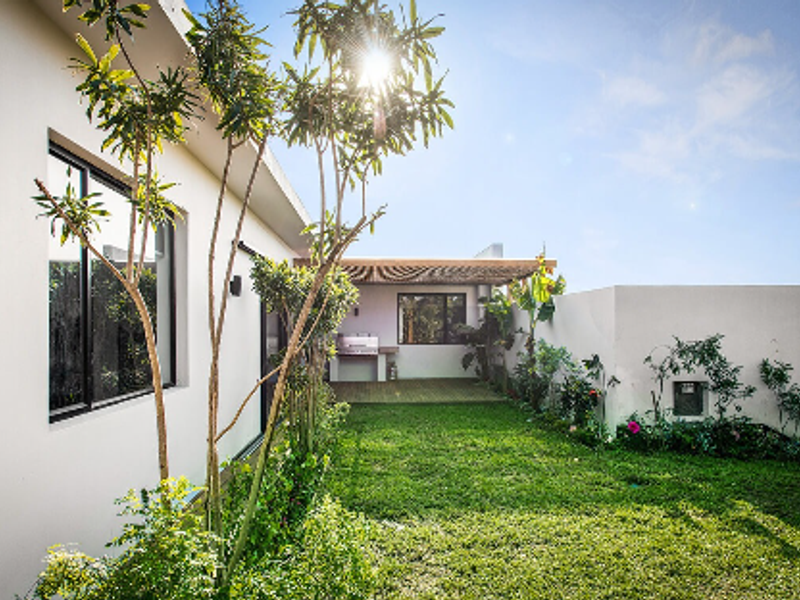 A well-maintained rear garden featuring a covered patio with a timber pergola, built-in braai, and direct access to the home via sliding glass doors.