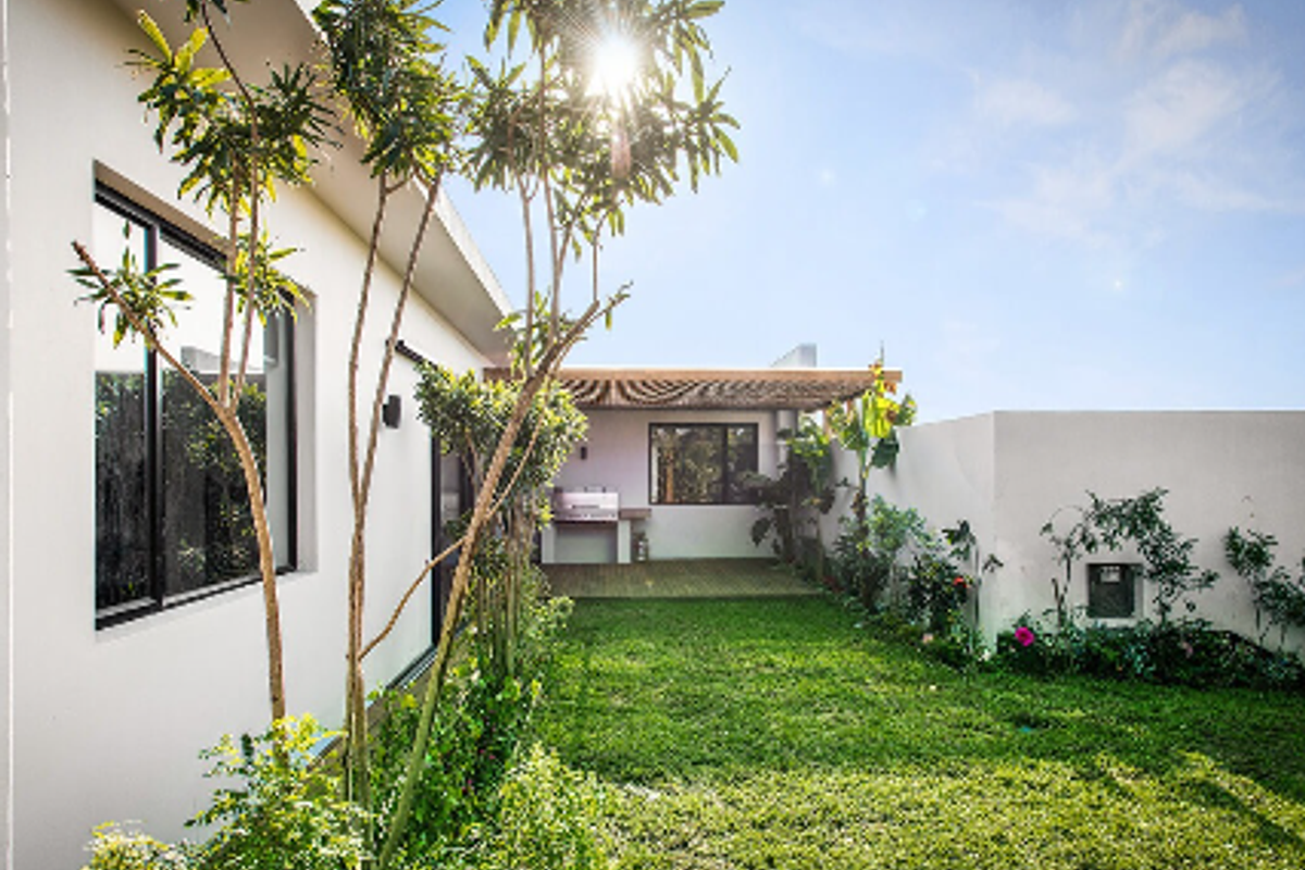 A well-maintained rear garden featuring a covered patio with a timber pergola, built-in braai, and direct access to the home via sliding glass doors.