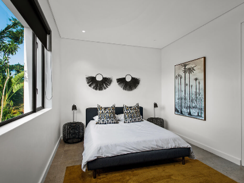 A modern, well-lit bedroom featuring neutral walls, tiled flooring, and a large window overlooking greenery.