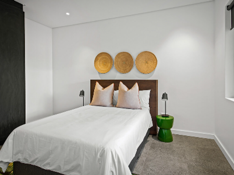 A modern, well-maintained bedroom featuring neutral walls, built-in cabinetry, recessed lighting, and a roller blind.