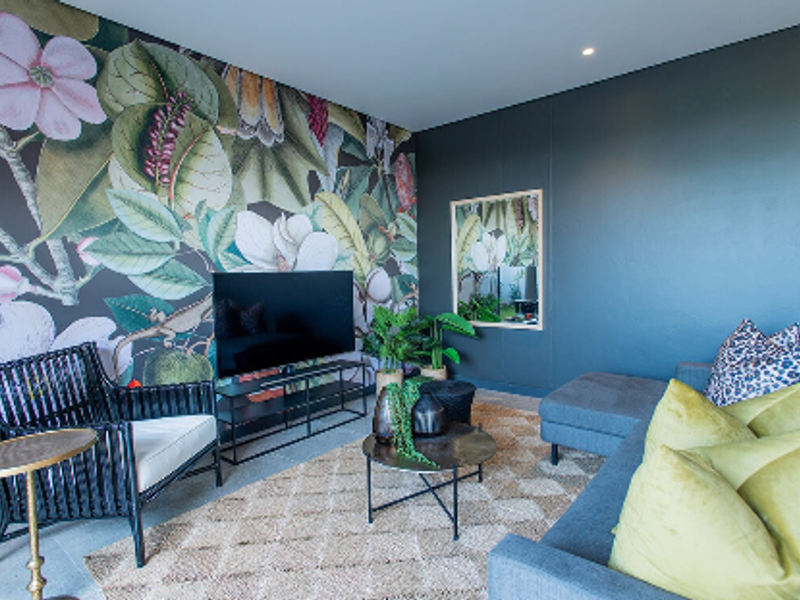 A modern living room featuring a bold floral feature wall, recessed downlighting, and a contemporary dark color palette.