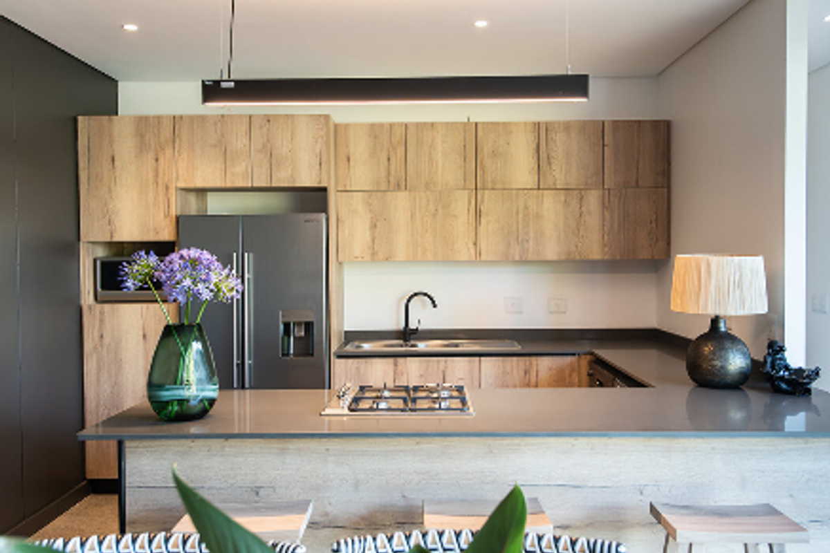 Modern kitchen featuring wood-grain cabinetry, stone countertops, a central gas hob, and sleek black fixtures in a well-lit, contemporary open-plan layout.