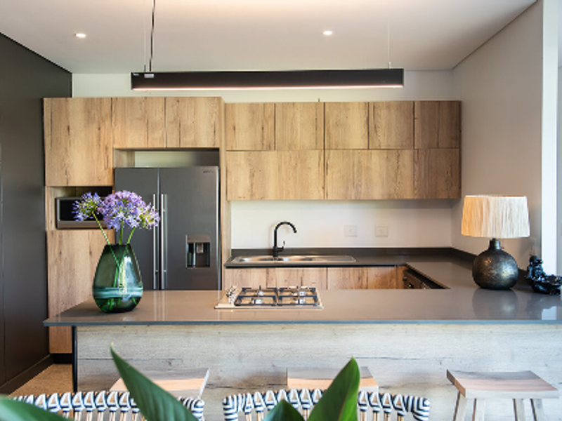 Modern kitchen featuring wood-grain cabinetry, stone countertops, a central gas hob, and sleek black fixtures in a well-lit, contemporary open-plan layout.