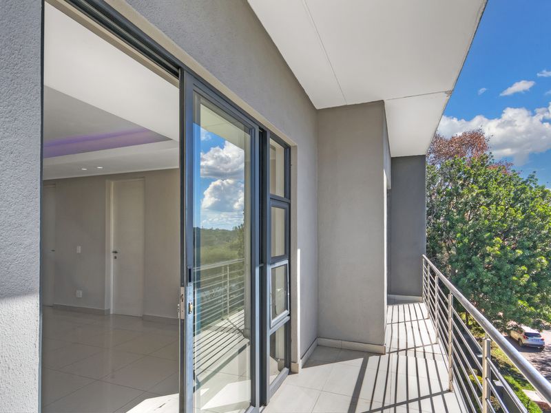 A modern, covered balcony featuring tiled flooring, a sleek stainless steel balustrade, and large sliding glass doors leading into the interior living space.