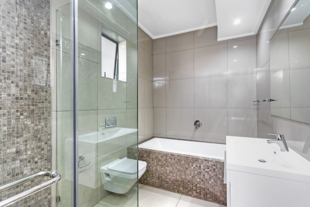 Modern bathroom featuring a glass-enclosed shower, wall-mounted toilet, built-in bathtub, and elegant mosaic tile accents with high-quality finishes.