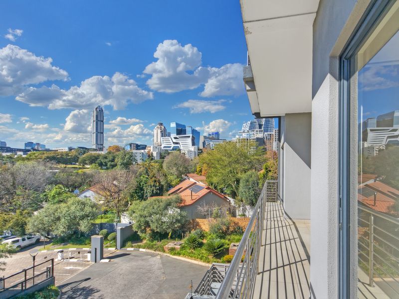 A clean, modern balcony featuring a metal balustrade and sliding glass door access, offering expansive views of the surrounding cityscape and neighborhood.