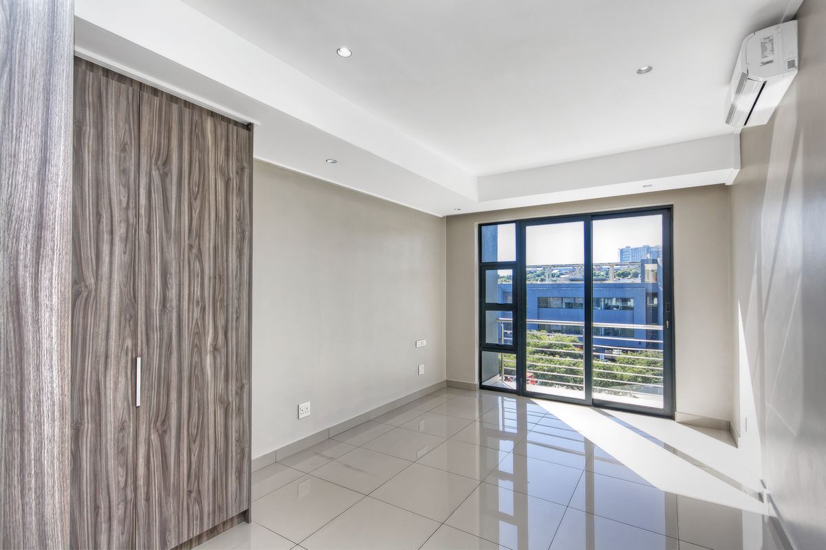A bright, modern bedroom featuring tiled floors, a built-in wardrobe, air conditioning, and a sliding glass door leading to a balcony.