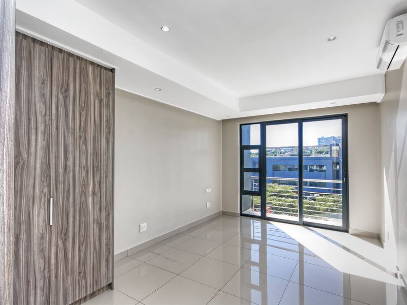 A bright, modern bedroom featuring tiled floors, a built-in wardrobe, air conditioning, and a sliding glass door leading to a balcony.