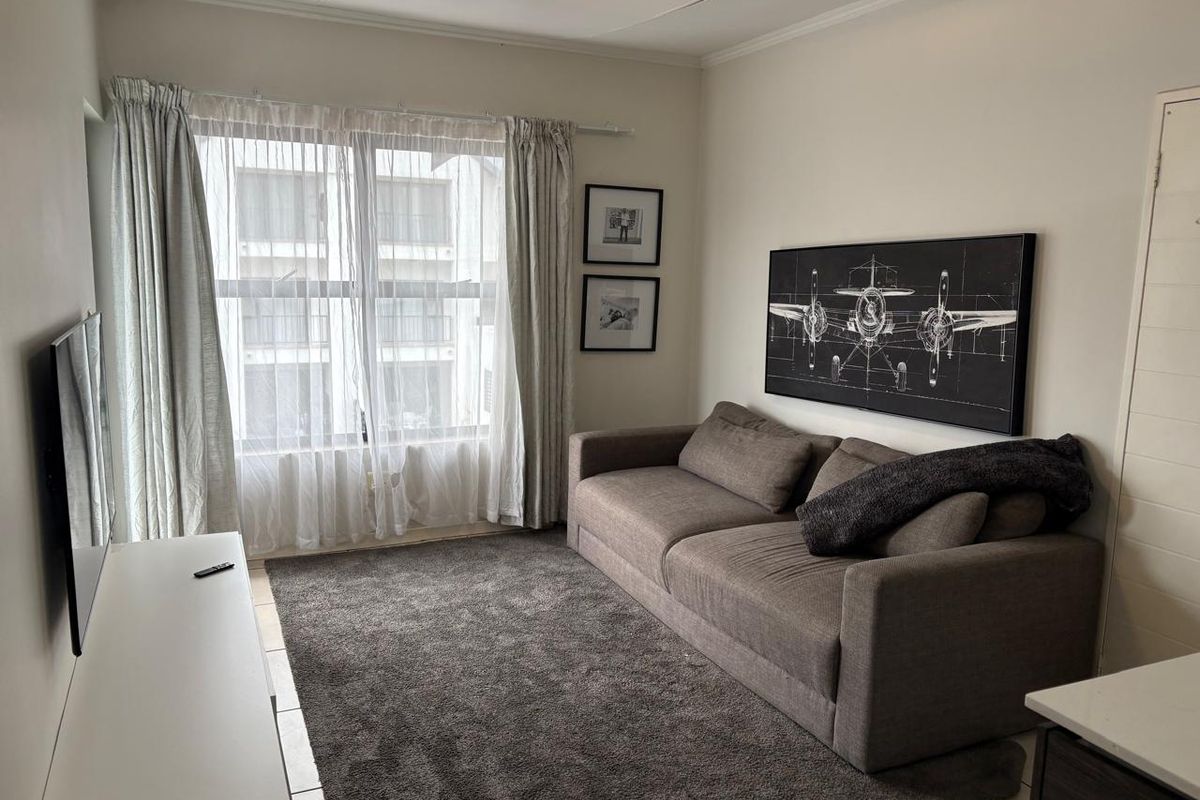 A comfortable living room featuring tiled flooring, neutral walls, and a large window that allows for natural light.