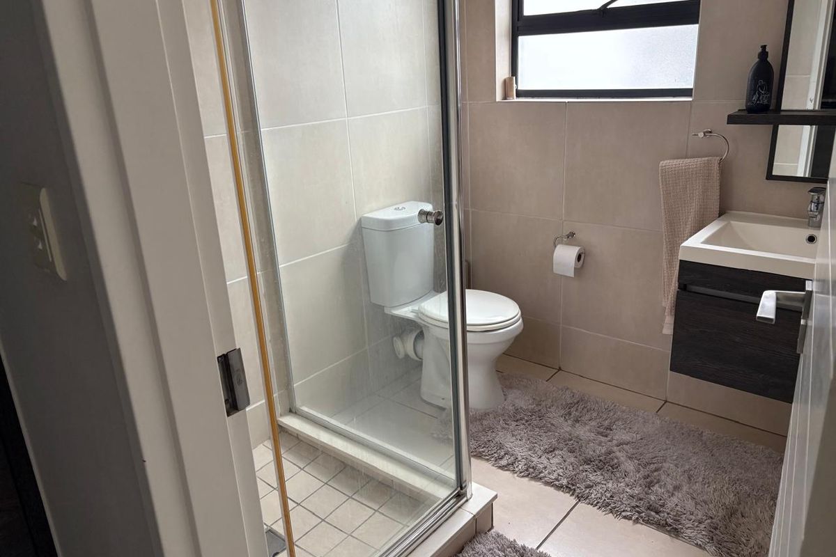 A modern bathroom featuring a glass-enclosed shower, a wall-mounted vanity with basin, and neutral floor-to-ceiling tiling.