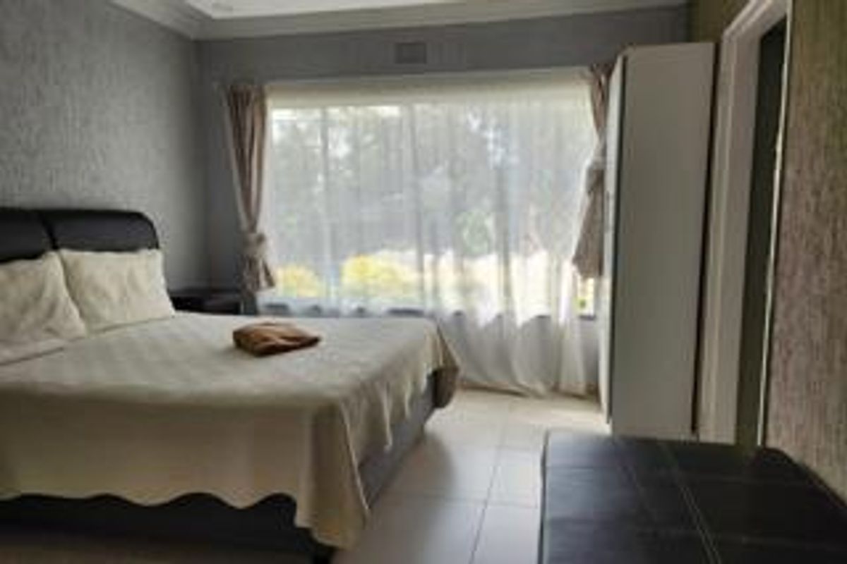 A bedroom featuring tiled flooring, a large window allowing natural light, and a built-in wardrobe for storage.