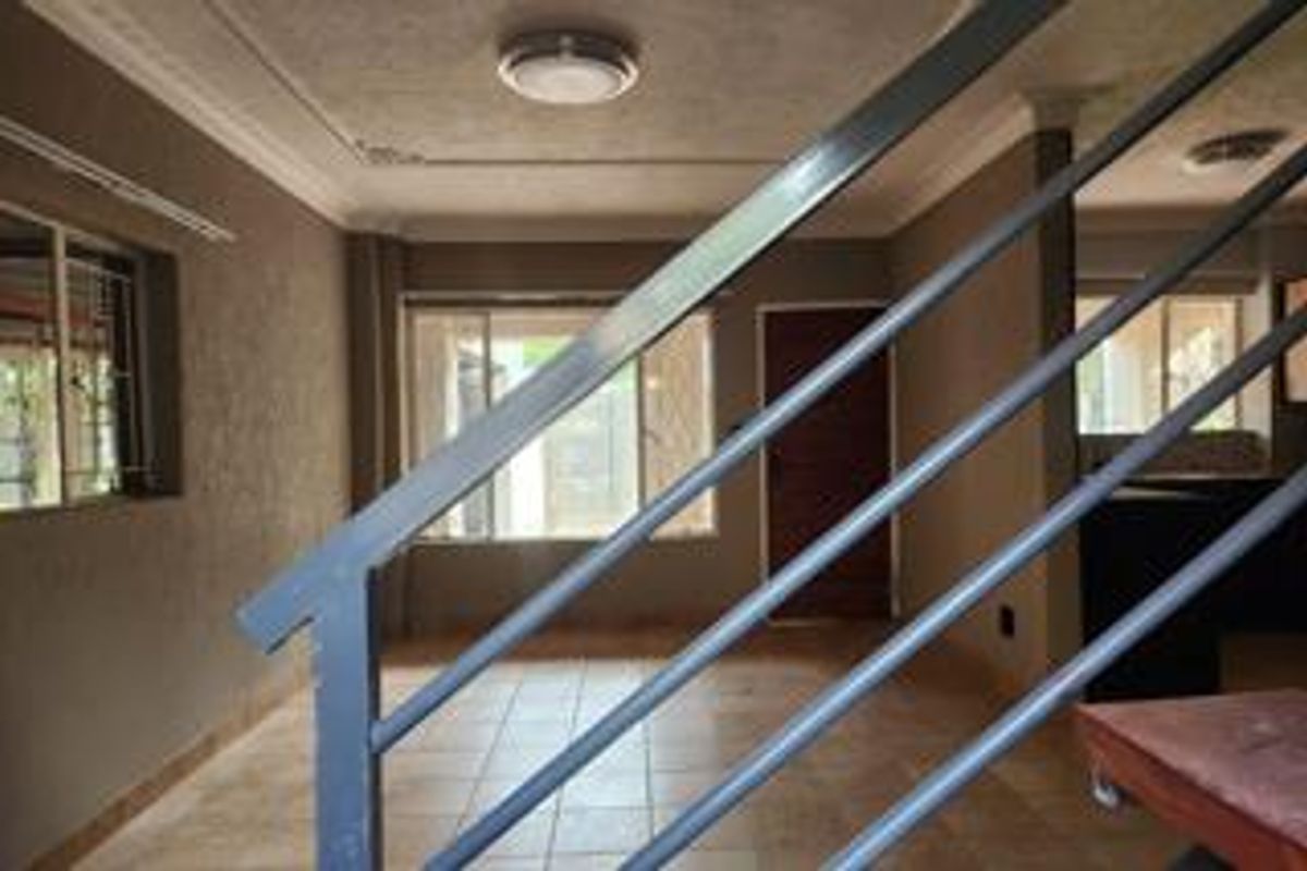 An open-plan living area featuring tiled flooring, a staircase with a metal railing, and neutral wall finishes, providing a blank canvas for interior design.