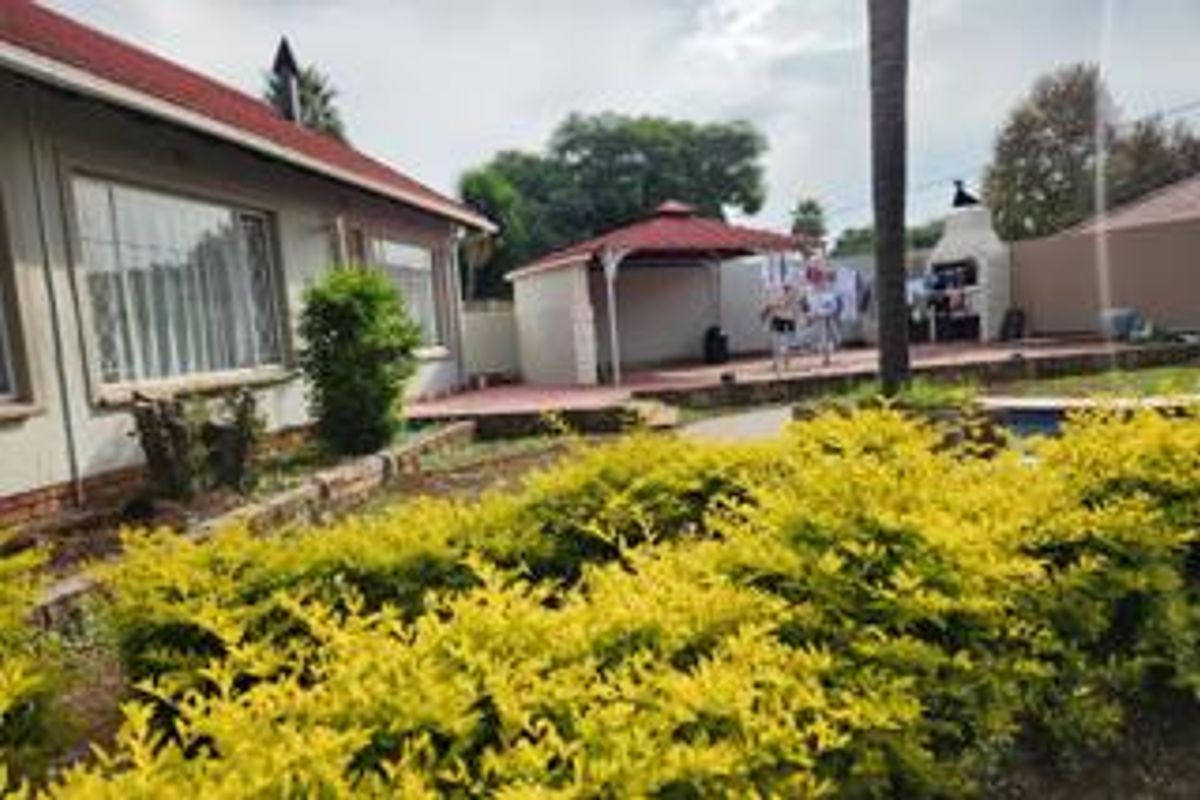 Rear exterior view featuring a paved patio area with a gazebo, built-in braai, and established garden landscaping.