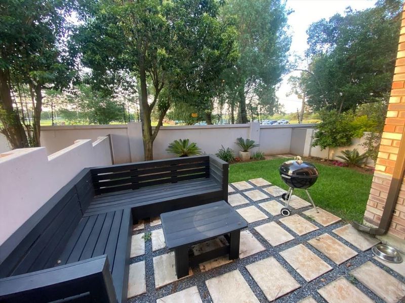 A private rear garden featuring a paved patio area, boundary wall, and established trees, providing a pleasant outdoor space for relaxation.