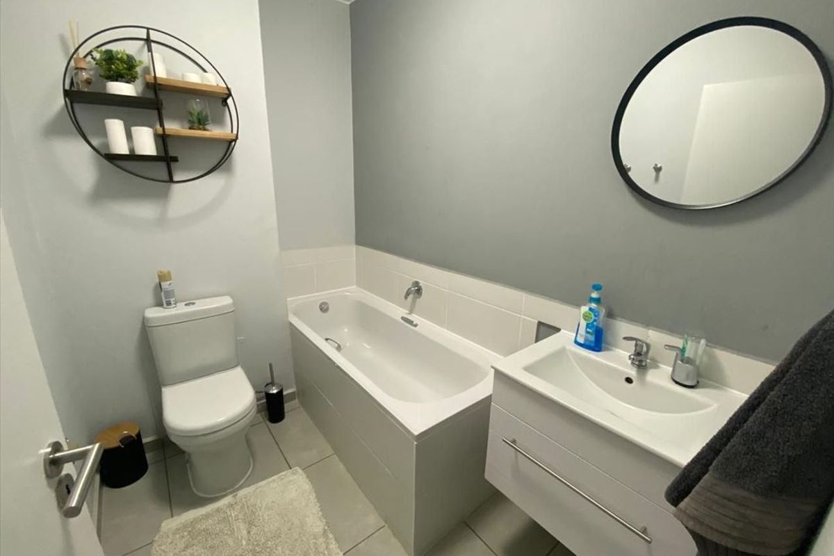 A modern bathroom featuring a built-in bathtub, a white vanity cabinet with a basin, and a toilet, finished with neutral wall tones and tiled flooring.
