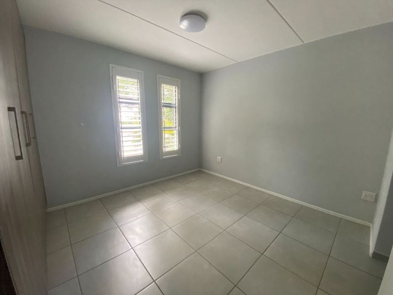 A clean, empty bedroom featuring neutral tiled flooring, built-in cupboards, and window shutters, providing a versatile space ready for personalization.