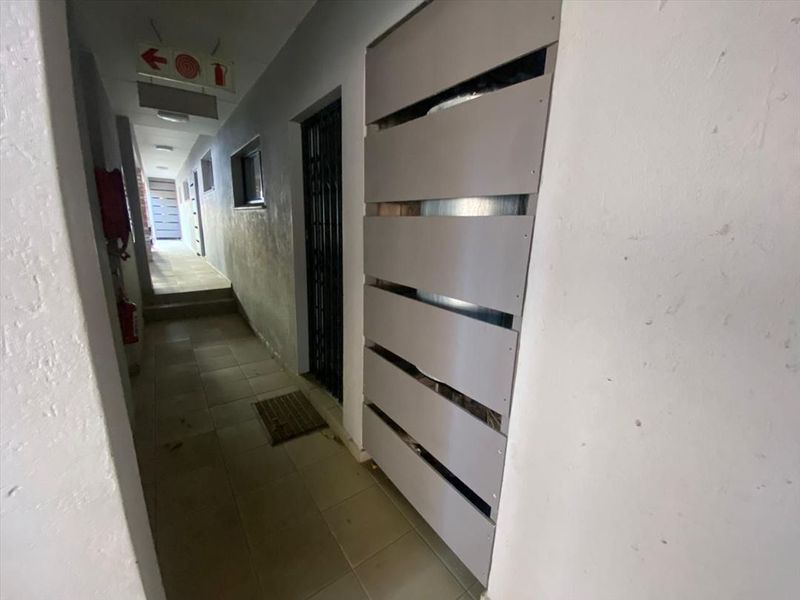 A functional communal hallway featuring tiled flooring, a security gate, and emergency safety equipment.