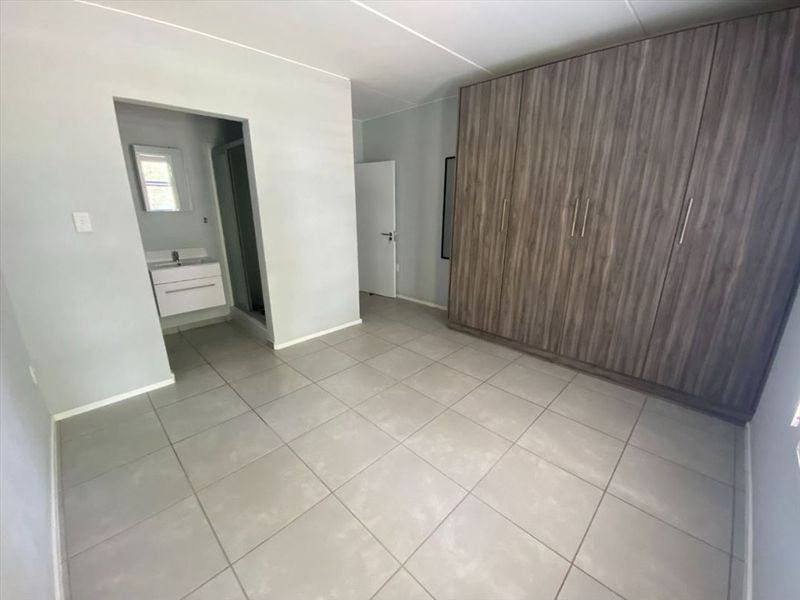 A spacious, empty bedroom featuring neutral tiled flooring, modern built-in cupboards, and direct access to an en-suite bathroom.