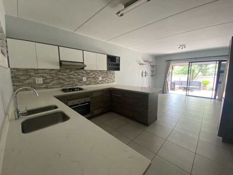 Open-plan kitchen and living area featuring modern cabinetry, stone countertops, built-in appliances, and sliding doors leading to an outdoor patio space.