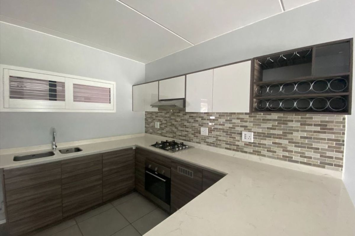Modern kitchen featuring stone countertops, mosaic tile backsplash, built-in gas hob, oven, extractor fan, and ample cabinetry with integrated wine storage.