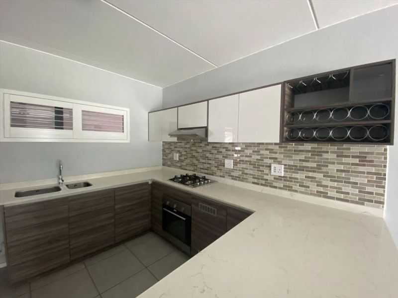 Modern kitchen featuring stone countertops, mosaic tile backsplash, built-in gas hob, oven, extractor fan, and ample cabinetry with integrated wine storage.