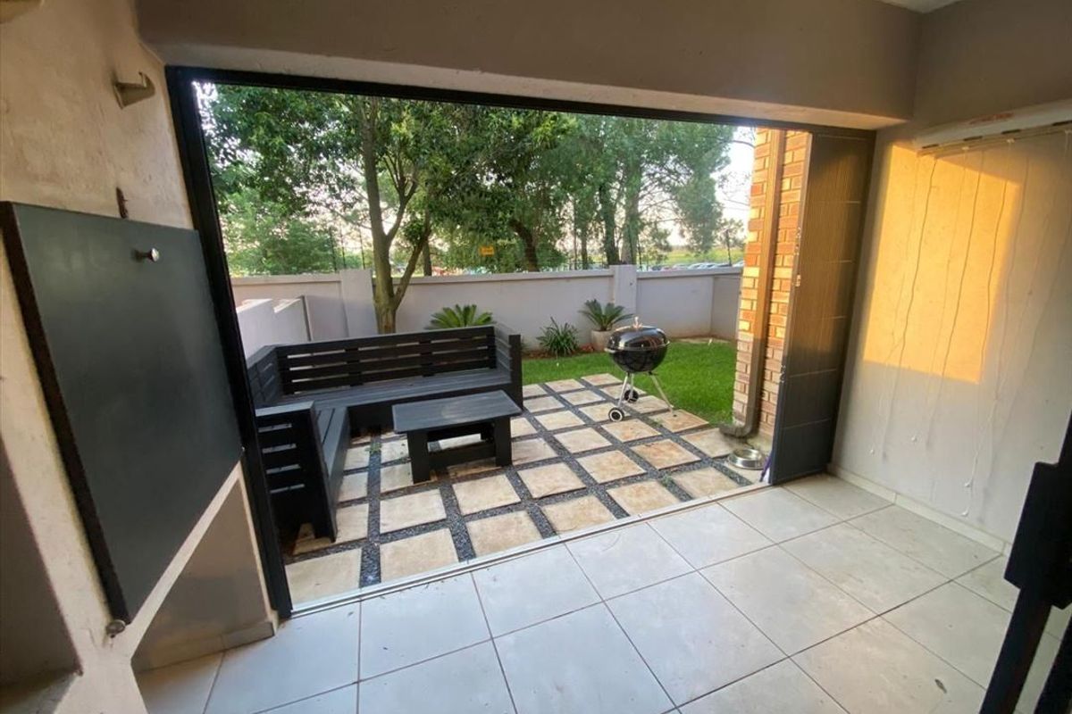 Covered patio area featuring a built-in braai, tiled flooring, and folding stack doors opening onto a paved garden space.