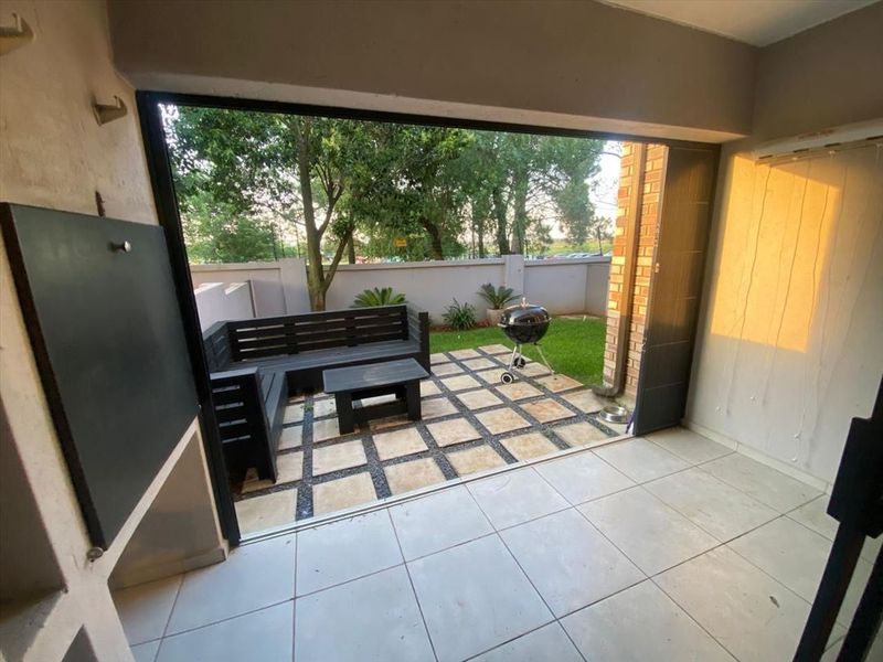 Covered patio area featuring a built-in braai, tiled flooring, and folding stack doors opening onto a paved garden space.