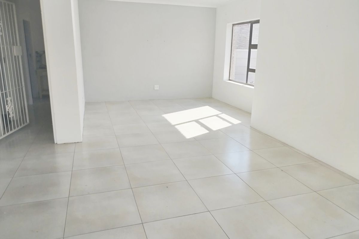 A bright, empty living area featuring neutral tiled flooring, clean white walls, and an aluminium-framed window, providing a blank canvas for interior design.