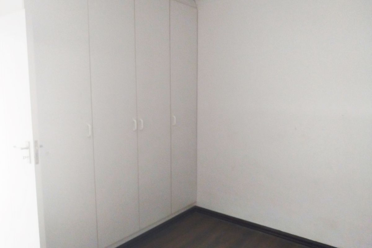 A clean, empty bedroom featuring neutral white walls, dark laminate flooring, and ample built-in cupboard storage.
