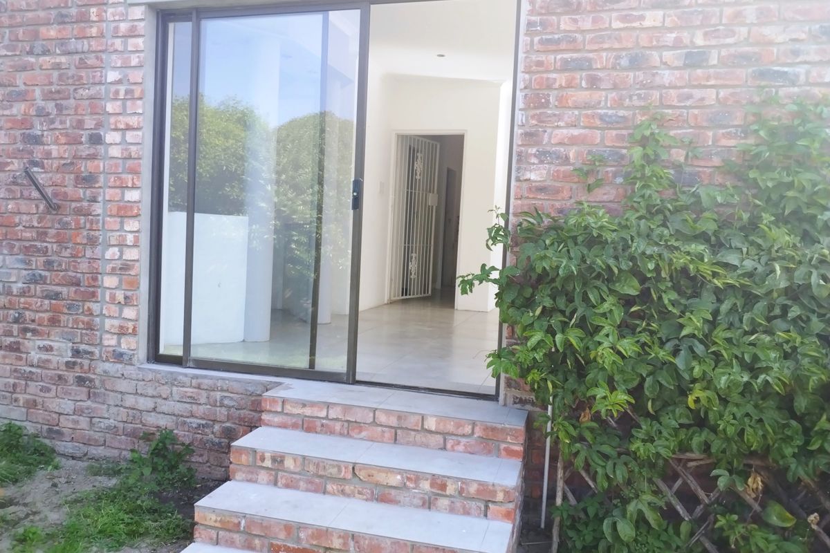 Rear exterior view of the apartment featuring an exposed brick facade, sliding glass door access, and brick steps leading into the interior.
