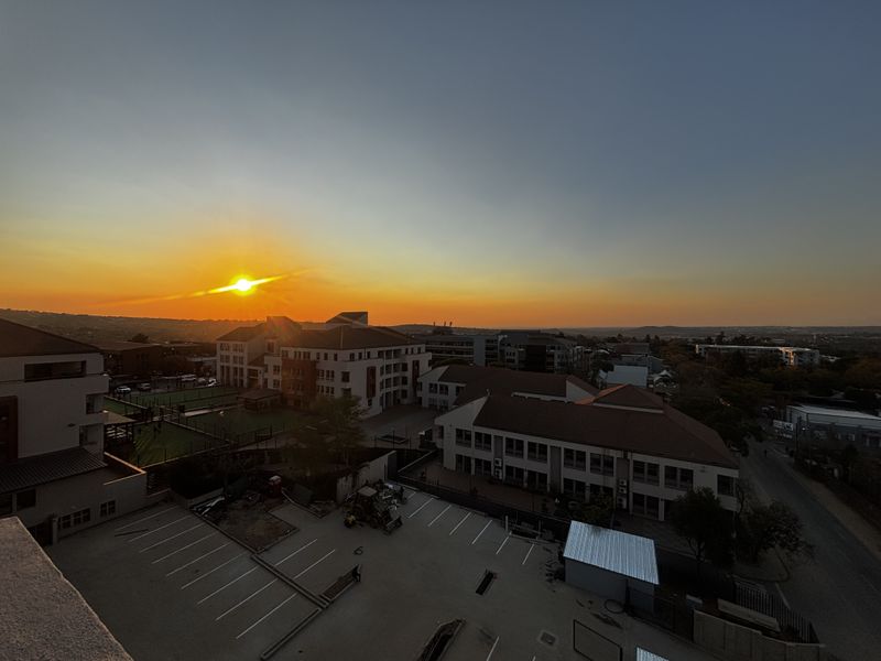 A scenic elevated sunset view overlooking the surrounding neighborhood, parking facilities, and nearby apartment complex buildings.