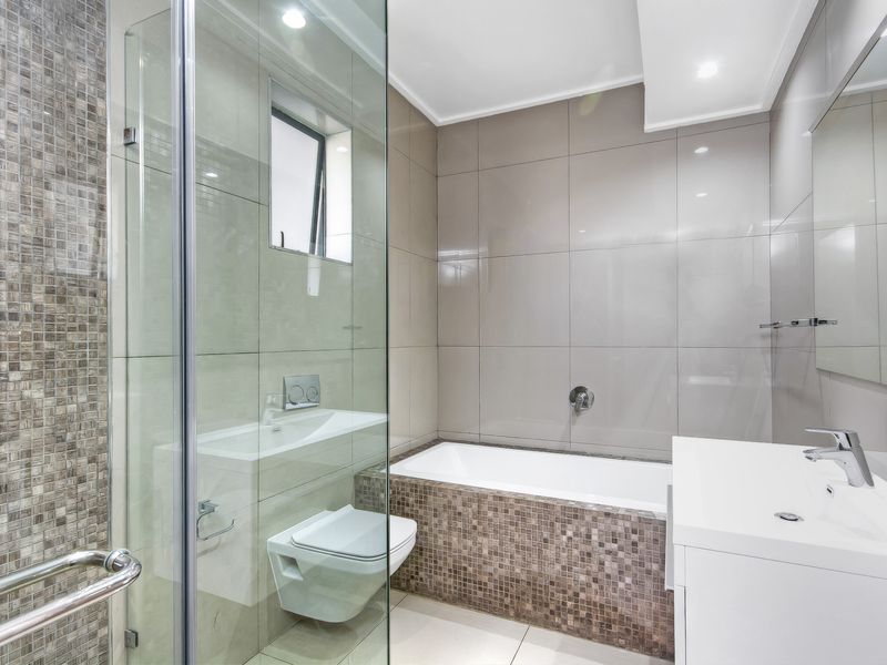 Modern bathroom featuring a glass-enclosed shower, wall-mounted toilet, built-in bathtub, and elegant mosaic tile accents with high-quality finishes.