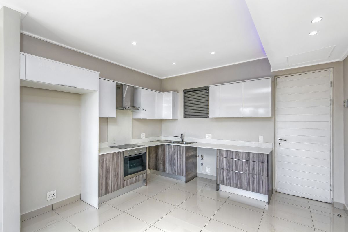 Modern kitchen featuring sleek two-tone cabinetry, built-in oven, electric hob, extractor fan, and polished porcelain floor tiles in a clean, contemporary layout.