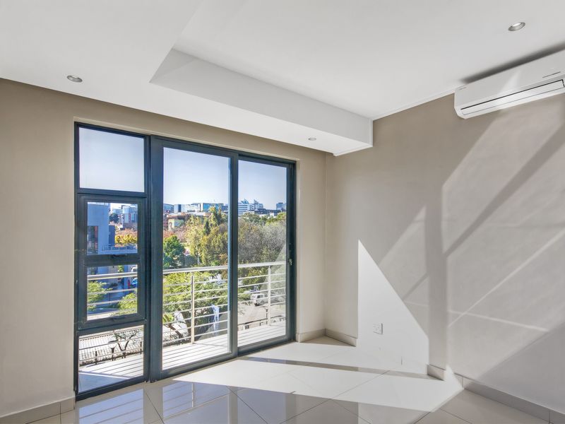 A bright, empty living area featuring tiled floors, recessed lighting, a wall-mounted air conditioner, and a sliding glass door leading to a balcony.