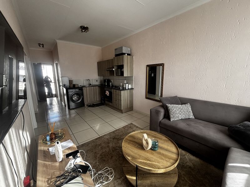 Open-plan living area featuring a compact kitchen with built-in cabinetry, oven, hob, and extractor fan, seamlessly connected to the lounge space.