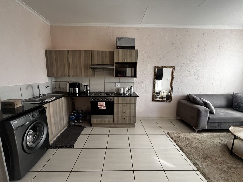 Open-plan living area featuring a compact kitchen with built-in cabinetry, oven, hob, and integrated laundry space, finished with neutral floor tiles.