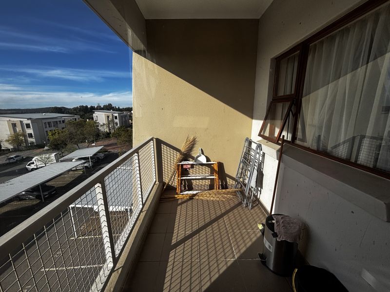 A functional apartment balcony featuring tiled flooring and a metal balustrade, offering an open-air space with views of the surrounding complex.