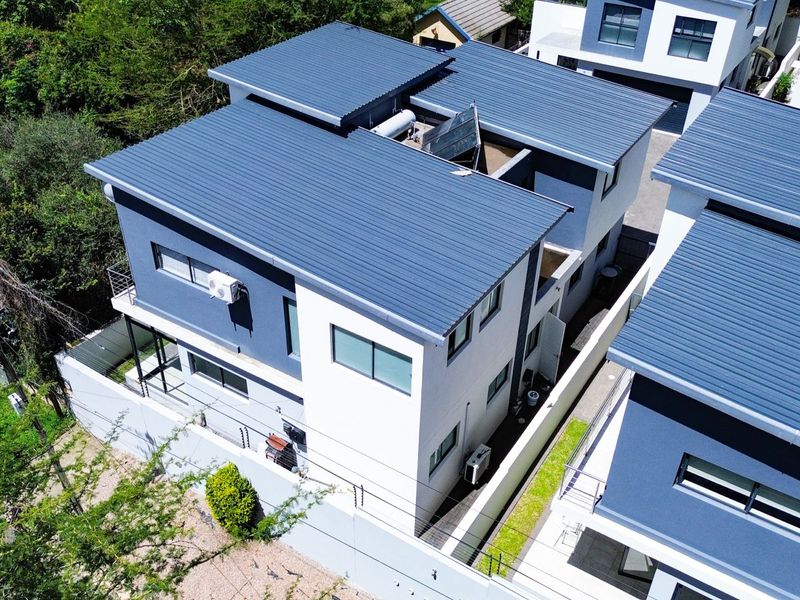 Aerial view of a modern cluster home featuring a corrugated metal roof, solar water heating system, and secure perimeter walling.