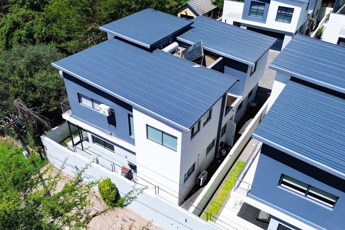 Aerial view of a modern cluster home featuring a corrugated metal roof, solar water heating system, and secure perimeter walling.