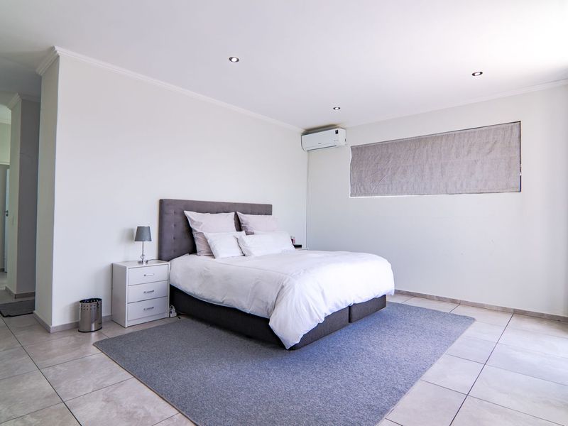 A spacious, well-maintained bedroom featuring neutral tiled flooring, recessed downlighting, and a wall-mounted air conditioning unit.