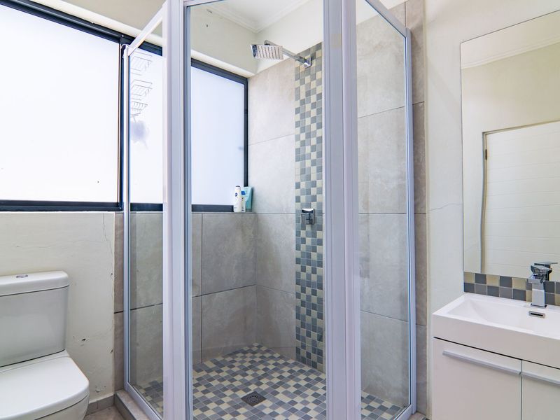 A functional bathroom featuring a glass-enclosed shower, modern vanity with basin, and tiled finishes, showing some signs of wear on the walls.