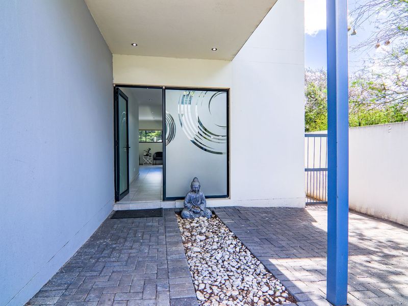 A modern entrance featuring a paved walkway with a decorative pebble bed, covered porch area, and a glass sliding door leading into the home.