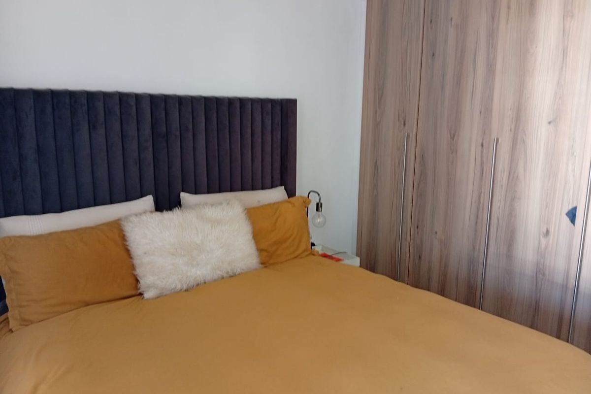 A well-maintained bedroom featuring a modern built-in wardrobe with wood-grain finish and a contemporary upholstered headboard.