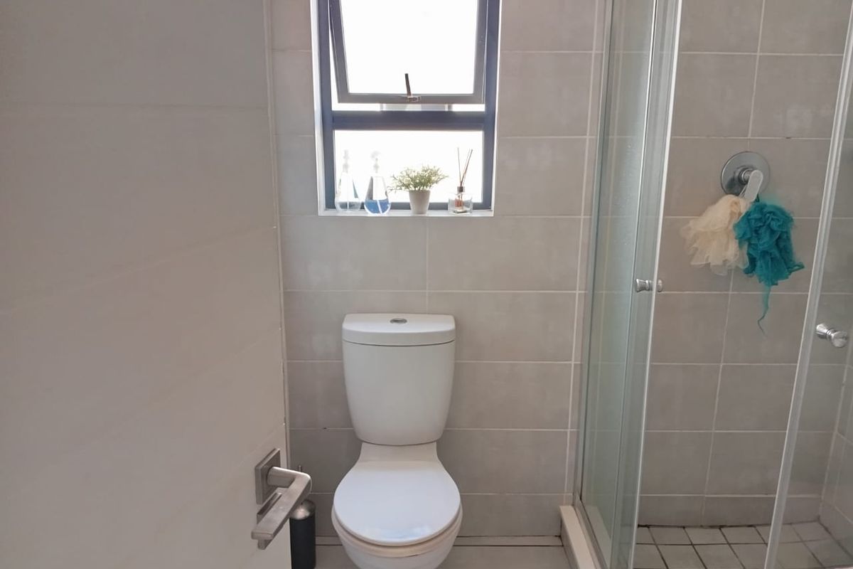 A functional bathroom featuring a modern toilet, a glass-enclosed shower, and neutral wall tiling with a top-hung window for natural light.