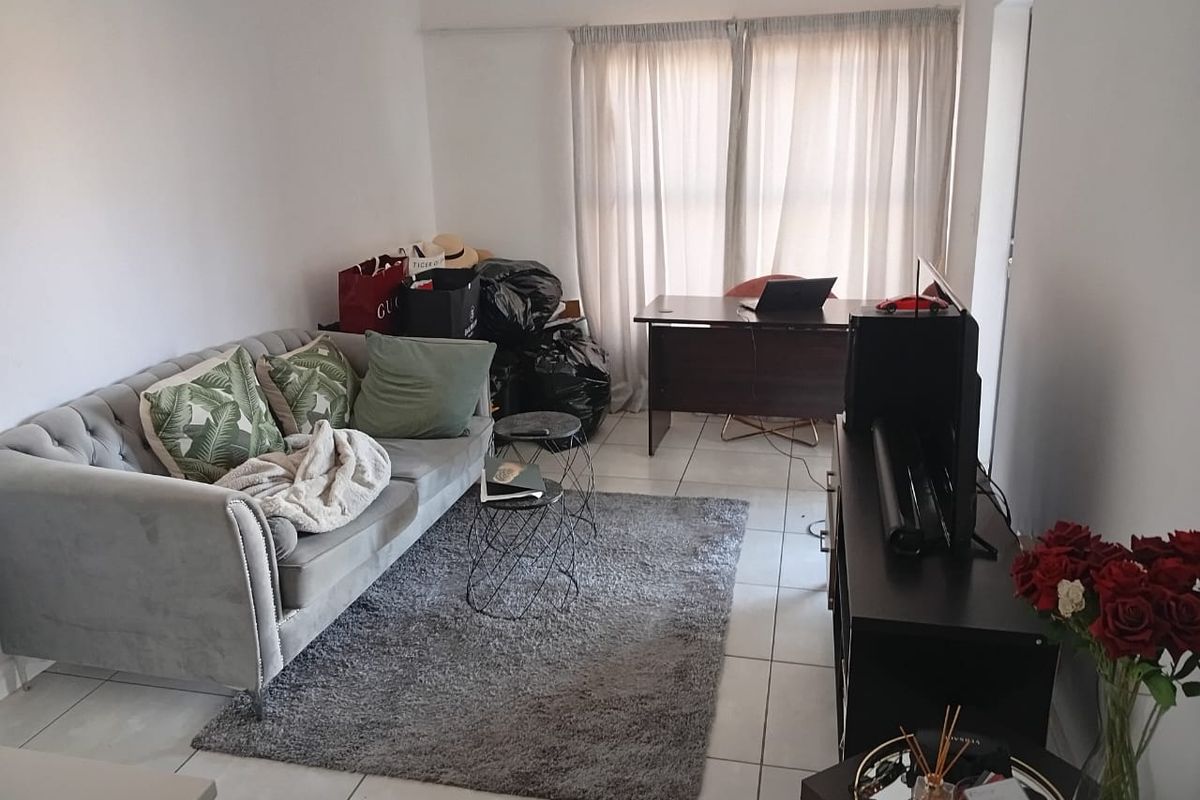 A functional living room area featuring neutral tiled flooring and large window access with installed curtain tracks.