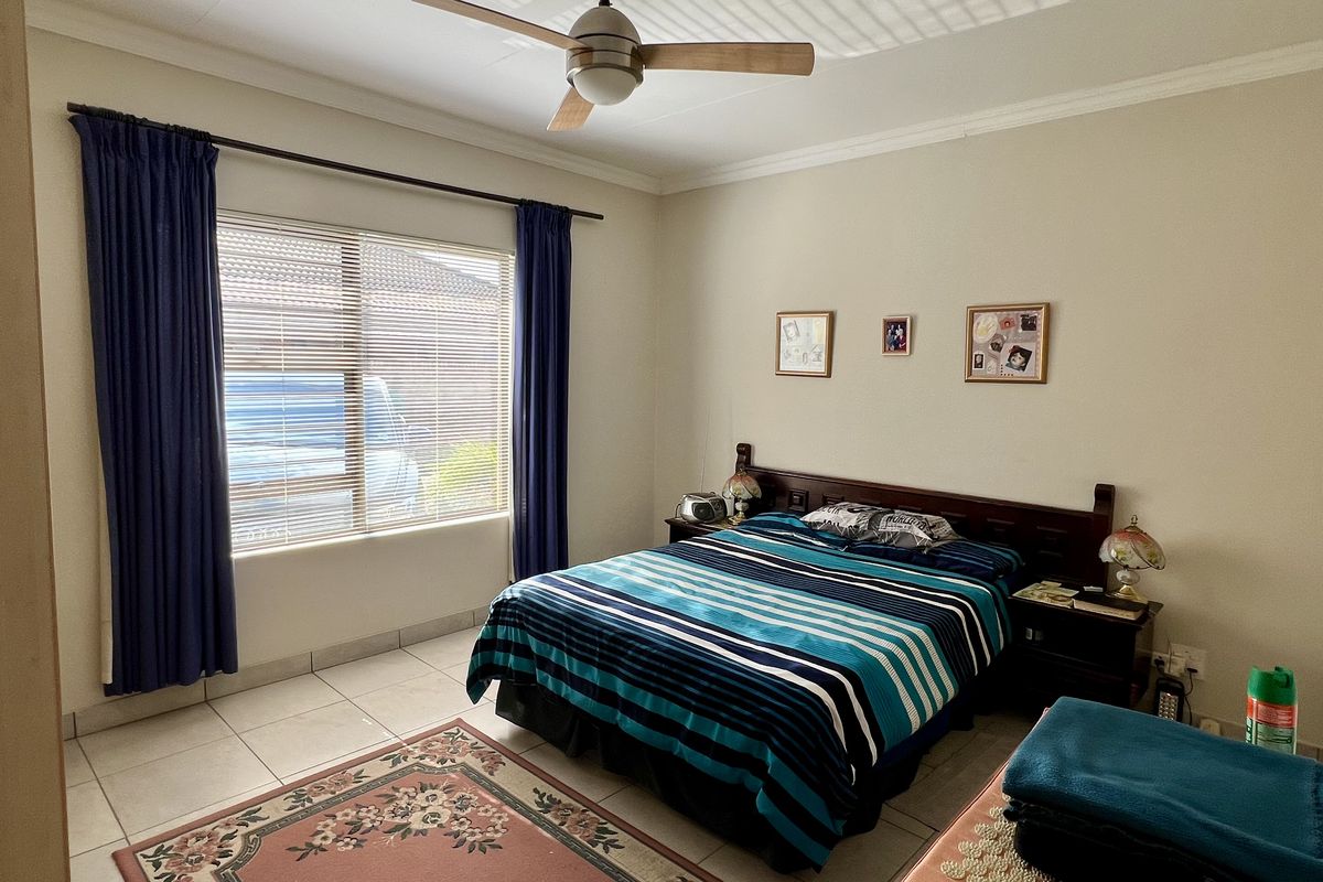 A functional bedroom featuring tiled flooring, a ceiling fan, and large windows with venetian blinds and curtain tracks.